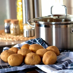 A bunch of raw unpeeled potatoes beside a large pot