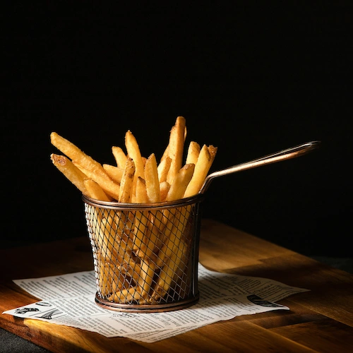 Shoestring Fries in a strainer under a spotlight in a dark room