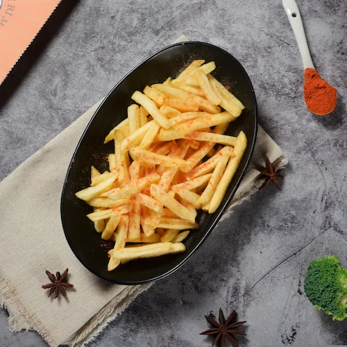 Spicy curry duck fat shoestring fries on a black plate surrounded by curry powder and broccoli